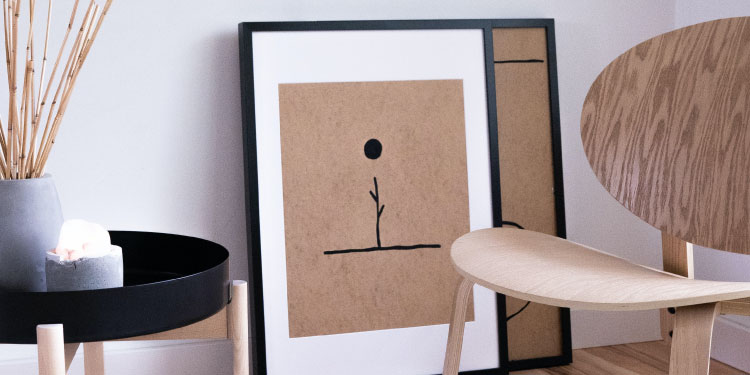 De gauche à droite : une petite table ronde et noir avec une bougie et un vase, 2 tableaux minimaliste posés contre le mur, une chaise en bois